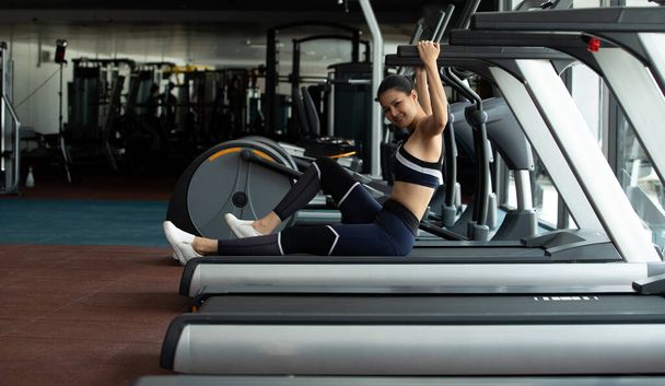 Asyalı ince spor kadın siyah saçlı spor sutyen beyaz ayakkabı egzersizi ısınıyor ve Fit Gym 'de koşu bandında yorgun oturuyor. Kavramsal kadın sporcu olabilir. Sağlıklı, kopyalama alanı. - Fotoğraf, Görsel
