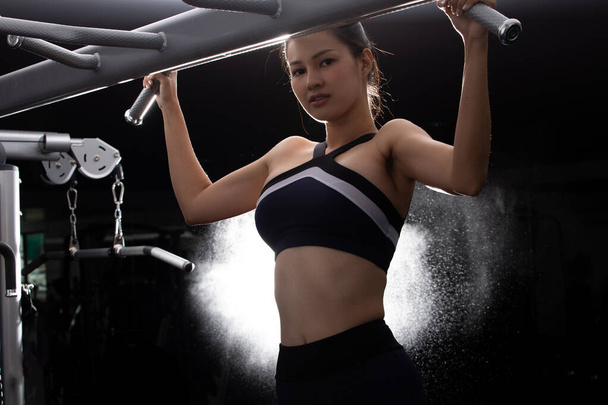 Aziatisch slank fitness vrouw zwart haar sport beha oefening opwarmen op Pull up machine gewicht spier handen armen bodybuilder in Fit Gym. Concept vrouw kan doen atleet Sport gezond, terug licht bokeh - Foto, afbeelding