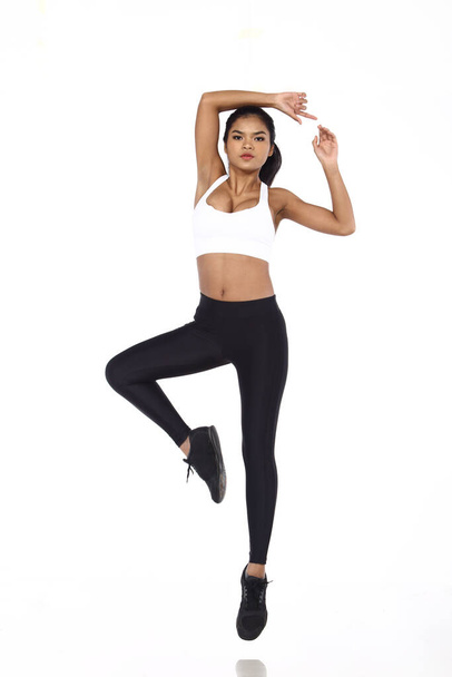 Asian Beautiful Fitness Girl in Sexy Cute Sport white Bra black spandex pants, wording "never give up" along line. Exercise warm up in white studio room, practice pose Jump one leg - Photo, Image