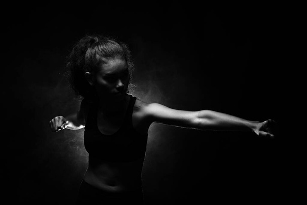 Asian Tan Skin Fitness Girl exercise boxing punch in Fog Smoke Dark background environment, studio lighting copy space b&w monotone color, concept Woman Can Do Sport, low exposure - Photo, Image