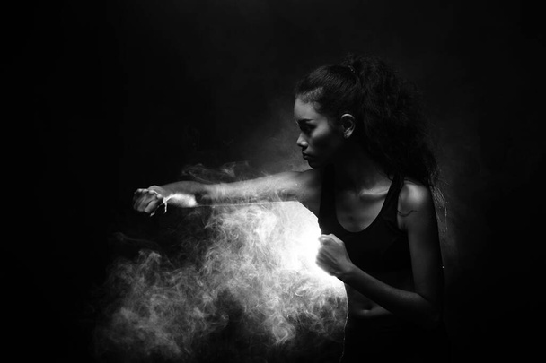 Asian Tan Skin Fitness Girl exercise boxing punch in Fog Smoke Dark background environment, studio lighting copy space b&w monotone color, concept Woman Can Do Sport, low exposure - Photo, Image
