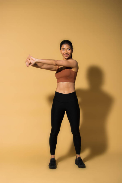 Азійська струнка жінка Фітнес тренується розігрівати розтягнені ноги рук, студія освітлює жовтий бежевий гірчичний фон простору тіней, концепція Жінка може робити атлетичні спортивні пачки 6 - Фото, зображення