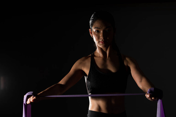 Азійська тонка фітнес-жінка тренує смугу опору розтягування рук в Fog Smoke Dark фонове середовище з низьким рівнем експозиції, студійне освітлення копіювання простору, концепцію Woman Can Do Sport 6 пачок - Фото, зображення