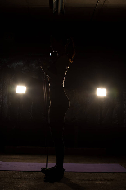 Азиатская стройная фитнес-женщина упражнения растяжения ног руки сопротивление браслет в тумане дыма Темный фон низкой экспозиции, студия освещения копировать пространство, концепция Женщина может делать спорт 6 пакетов
 - Фото, изображение