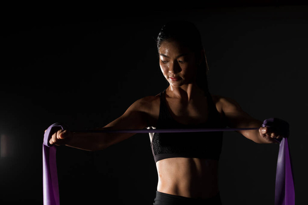 Ázsiai vékony Fitness nő gyakorlása nyújtózkodó lábak kar ellenállás szalag Fog füst Sötét háttér alacsony expozíciós környezet, stúdió világítás fénymásolás tér, koncepció Woman Can Do Sport 6 csomag - Fotó, kép