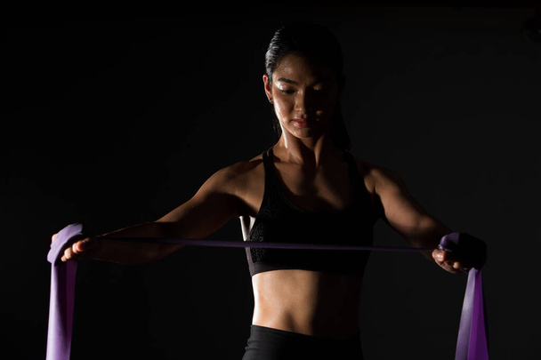 Азійська тонка фітнес-жінка тренує смугу опору розтягування рук в Fog Smoke Dark фонове середовище з низьким рівнем експозиції, студійне освітлення копіювання простору, концепцію Woman Can Do Sport 6 пачок - Фото, зображення