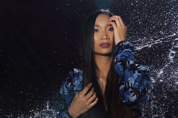 Beautiful Active fitness Asian Tanned Woman blue rain coat with Water Splash over studio lighting black backgrounds copy space for text logo, no retouch, concept water festival - Φωτογραφία, εικόνα