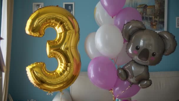 Verjaardags ballonnen in een heldere kamer. Ballonnen opgeblazen met helium, zwaaien lichtjes aan een touw. Gouden nummer 3 en bruine beer. Sluiten. - Video