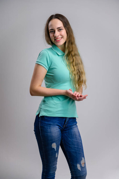 Vertical photo of a smiling pretty young woman with long hair in a turquoise blue jeans blouse on a white background. - Foto, afbeelding