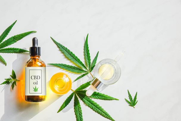Glass brown bottle with cannabis CBD oil with label and marijuana leaves on a marble background. Copy space - Photo, Image