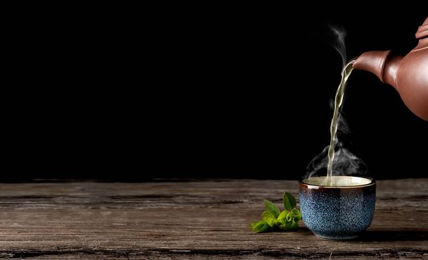 熱い緑茶は青のボウルにティーポットから注がれ、ヴィンテージの木製のテーブルは、カップの上に蒸気が上昇します。お茶のカップの横に残します。クローズアップ、茶道、ミニマリズム、テキスト用のコピースペース. - 写真・画像