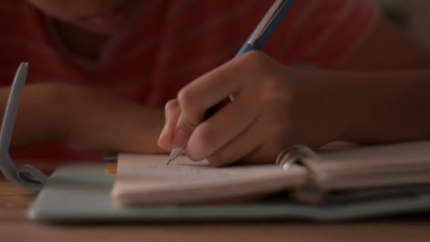 Закрыть руку маленькой девочки, пишущей на блокноте. Женщина-школьница делает записи в дневнике. Делать домашнее задание с письменным материалом. Концепция образования
. - Кадры, видео