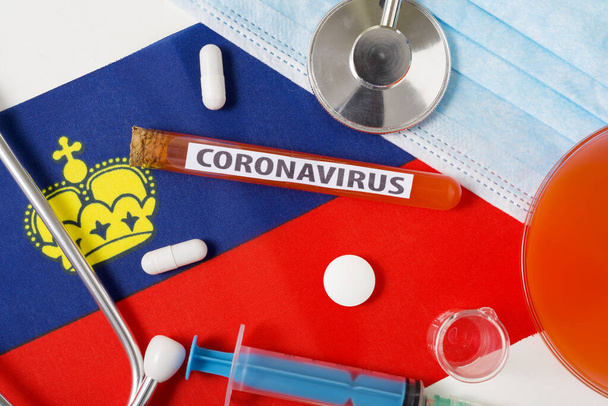 Coronavirus, nCoV koncept. Horní pohled ochranná dýchací maska, stetoskop, injekční stříkačka, tablety na vlajce Lichtenštejnska. Nový výskyt čínského koronaviru - Fotografie, Obrázek