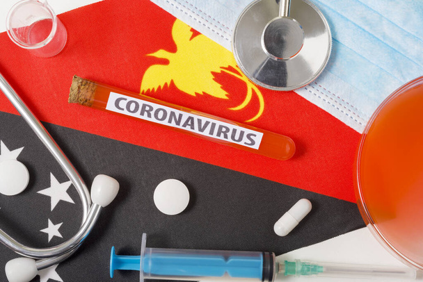 Coronavirus, nCoV concept. Top view protective breathing mask, stethoscope, syringe, tablets on the flag of Papua New Guinea. A new outbreak of the Chinese coronavirus - 写真・画像