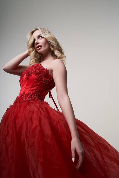 Young blonde in red dress looking at side in studio - Foto, afbeelding