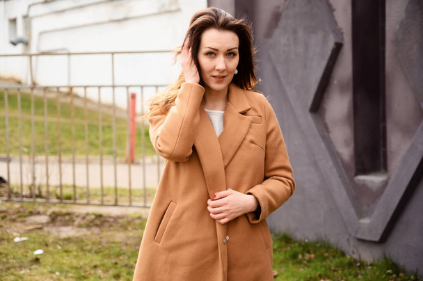Portrait of a brunette girl standing in spring in a beige coat walk a street against the backdrop of the city - Fotografie, Obrázek