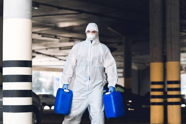 Vírusvédőruhás férfi, aki két kanna fertőtlenítőszert tart. - Fotó, kép