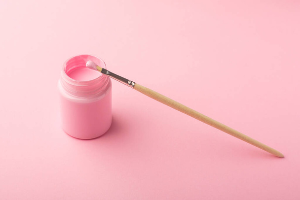 Pink acrylic paint with a brush on pink background, simple pastel composition side view - 写真・画像