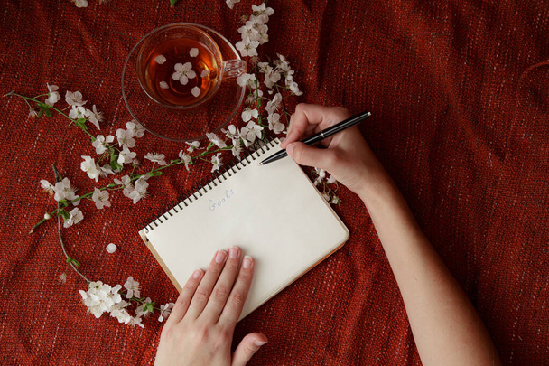 Kadının elleri dizaynınız için kalem ve spiral not defteri tutuyor. Kırmızı arka plan, düz yatış tarzı. Bahar fikri ve konsepti, değişim, bir dilek tutmak ve hedefler belirlemek - Fotoğraf, Görsel