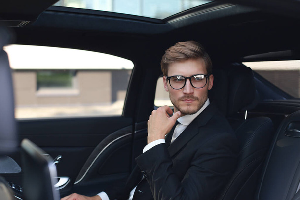 Przemyślany pewny siebie biznesmen w pełnym kolorze z okularu patrząc z dala siedząc w samochodzie - Zdjęcie, obraz