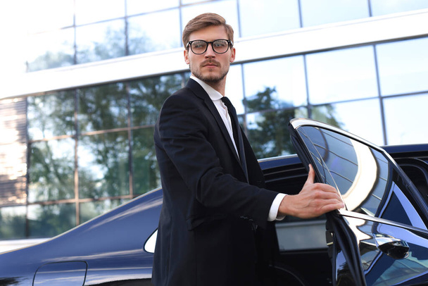 Κομψός νεαρός επιχειρηματίας εισέρχεται στο αυτοκίνητό του ενώ στέκεται σε εξωτερικούς χώρους - Φωτογραφία, εικόνα