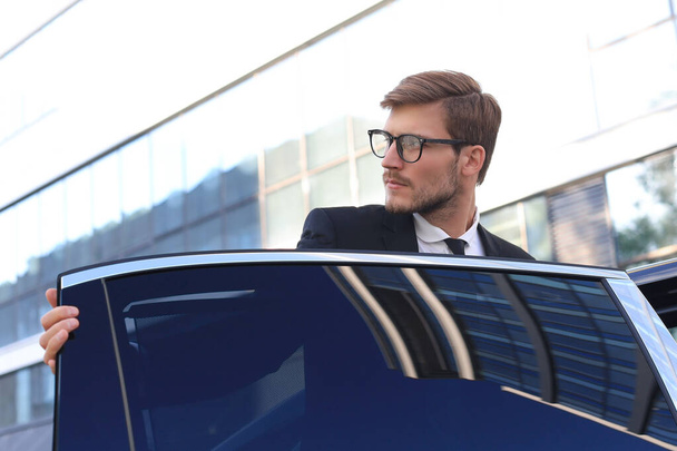 Tyylikäs nuori liikemies astuu autoonsa seistessään ulkona
 - Valokuva, kuva