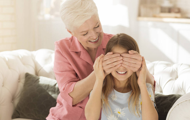 Игра Угадай, кто. Веселая пожилая леди закрывает глаза внучкам, делает сюрприз дома
 - Фото, изображение