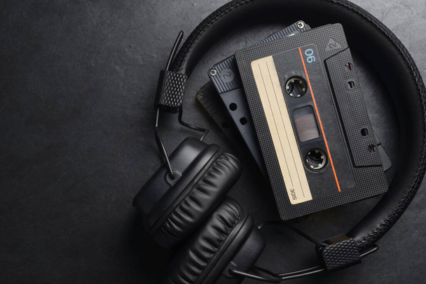 Μαύρα ακουστικά στο αυτί και ταινίες ήχου συμπαγείς κασέτες σε φόντο σχιστόλιθου - Φωτογραφία, εικόνα
