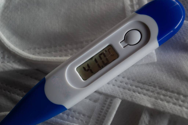 Ein medizinisches Thermometer, das die hohe Temperatur auf der Gesichtsmaske anzeigt - Coronavirus - Foto, Bild