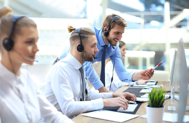 Portrait of call center worker accompanied by his team. Smiling customer support operator at work - Фото, изображение
