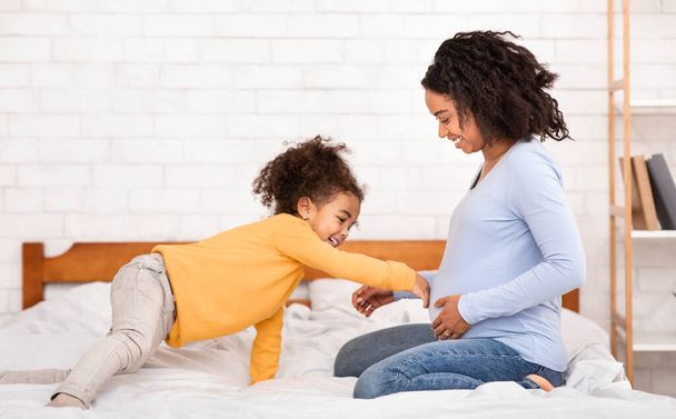 Little Girl Touching Moms Pregnant Belly Sitting In Bed Indoor - Foto, Imagen