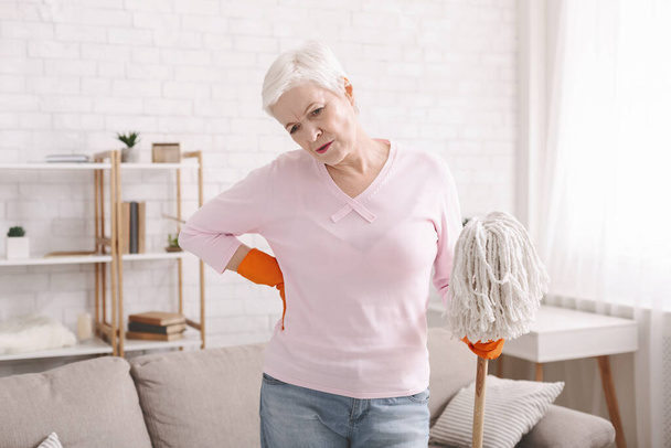 Cansada mulher idosa sofrendo de dor nas costas limpeza em casa
 - Foto, Imagem