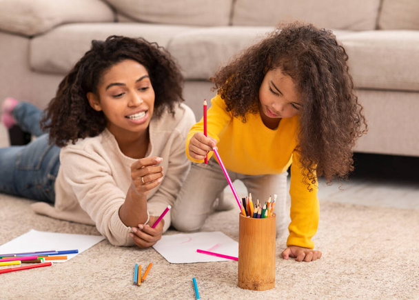 Schwarze Mutter und kleine Tochter skizzieren auf dem Boden liegend drinnen - Foto, Bild