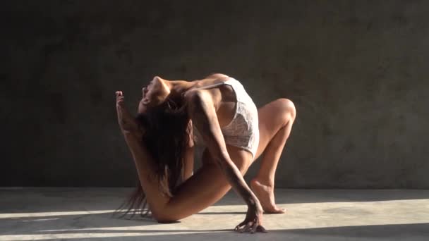 Schöne Akrobatik in weißen Spitzenunterwäsche, die im Studio über Betonwänden tanzt - Video in Zeitlupe - Filmmaterial, Video