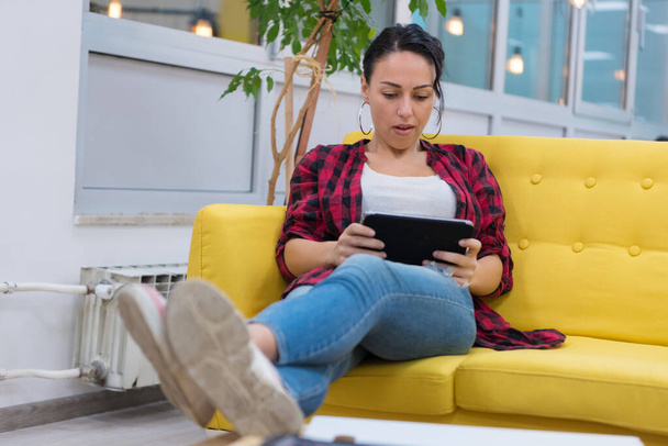 Young American business woman sitting at her sofa, using tablet in her office. - Foto, imagen