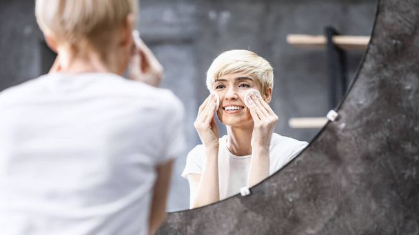 Lady quitando maquillaje usando almohadillas de algodón en el baño en casa
 - Foto, Imagen