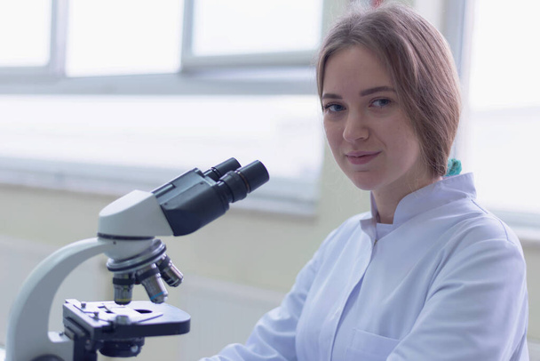 研究室で顕微鏡を見ている若い女性科学者微生物学的解析医学. - 写真・画像