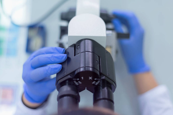 Jeune scientifique regardant à travers un microscope dans un laboratoire faisant de la recherche, analyse microbiologique, médecine. - Photo, image