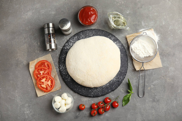 Flat lay composition with dough and fresh ingredients for pizza on grey table - Valokuva, kuva