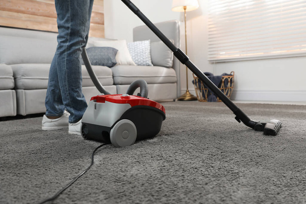 Young man using vacuum cleaner at home, closeup - Фото, изображение