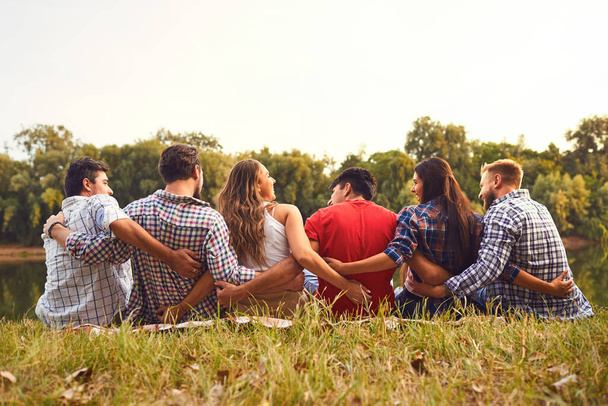 Young people sit on the grass hugging in nature in the park - Фото, изображение