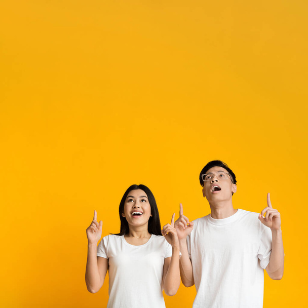 Verbazingwekkende aziatische man en vrouw wijzen omhoog naar de vrije ruimte - Foto, afbeelding