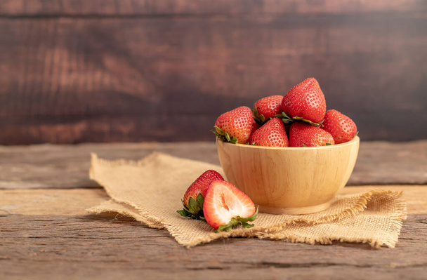 Strawberries are in a bowl on a brown sack placed on the wooden table. - Photo, Image