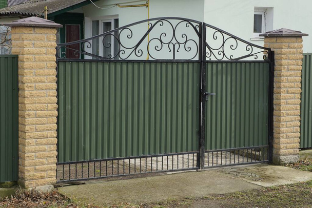 1つの大きな緑色の金属製の門と通りの茶色のレンガ造りの柵の一部 - 写真・画像