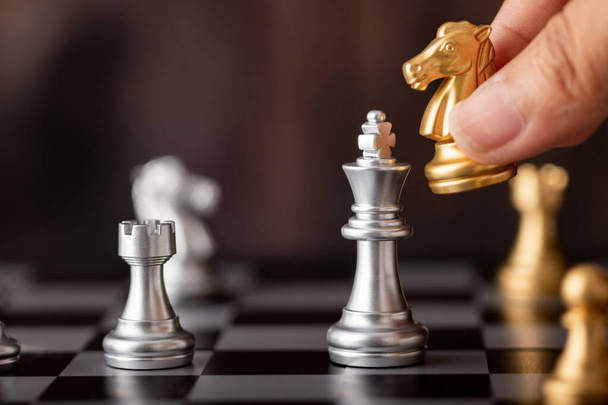 Hand hält Goldpferd Angriff Silberkönig im Spiel auf dem Schachbrett mit Holzhintergrund - Foto, Bild