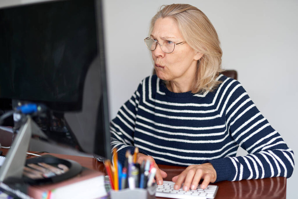 Серьезный зрелый среднего возраста в очках с помощью ноутбука печатают электронную почту, работая в домашнем офисе, дама ищет информацию в Интернете или общаться в Интернете
 - Фото, изображение