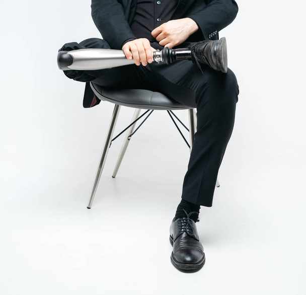 Gedeeltelijk zicht op gehandicapte jongeman met kunstbeen zittend op een stoel in de studio, kunstmatig ledemaat concept over witte achtergrond - Foto, afbeelding