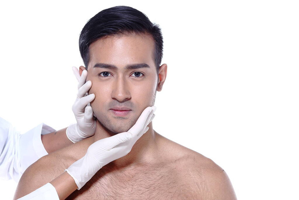 Asian man want to check eye, nose, eyebrow, forehead, cheek, jawline before plastic surgery, touch by nurse's rubber gloves, studio lighting white background copy space for text logo - Photo, Image