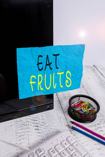 Conceptual hand writing showing Eat Fruits. Business photo showcasing consume any product of plant growth useful to humans or animals Note paper taped to black screen near keyboard stationary. - Photo, Image