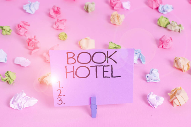 Handwriting text writing Book Hotel. Concept meaning an arrangement you make to have a hotel room or accommodation Colored crumpled papers empty reminder pink floor background clothespin. - Photo, Image